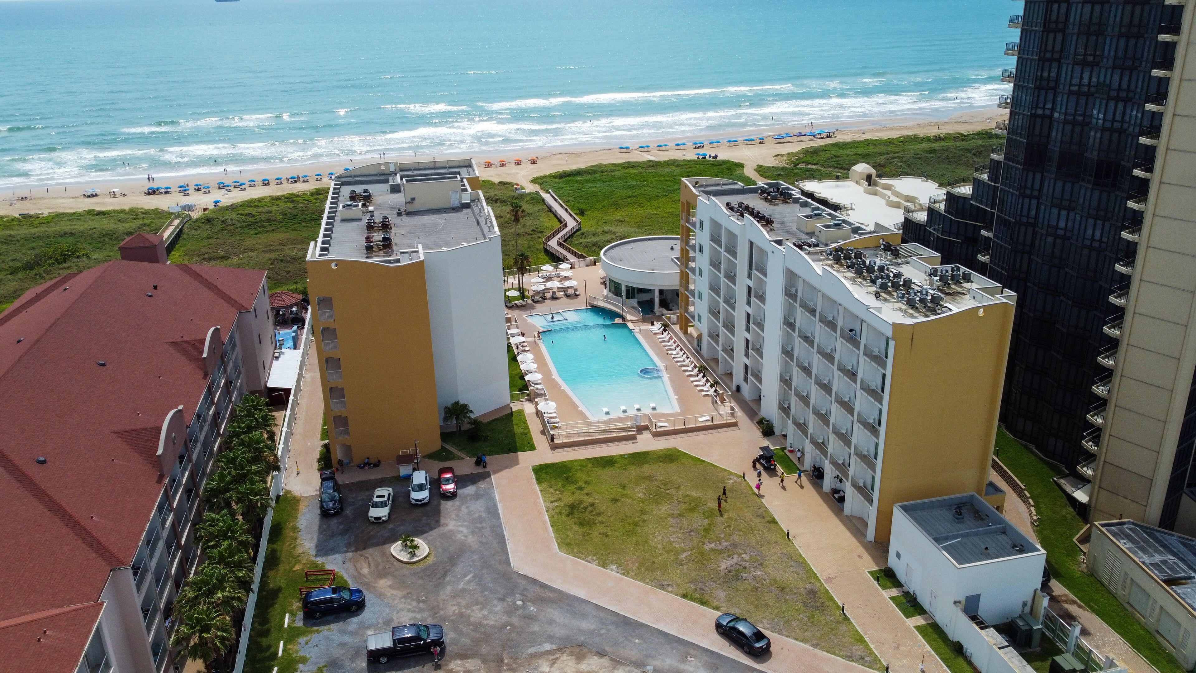 A high-rise hotel with a rooftop pool, a beach view, and a parking area.