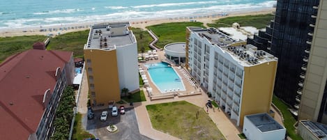 Un hotel de gran altura con piscina en la azotea, vistas a la playa y un área de estacionamiento.