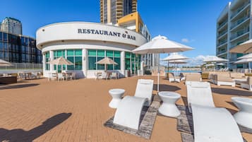 A restaurant and bar with outdoor seating, including sun loungers and umbrellas, and a pool area with lounge chairs.