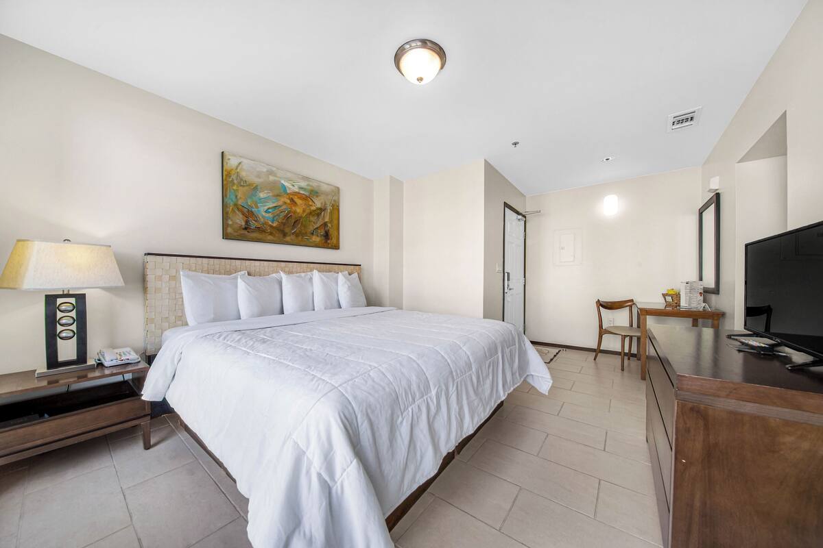 Une chambre d’hôtel avec un grand lit, un bureau, une chaise, une télévision, une lampe et un tableau au mur.