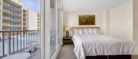 A hotel room with a balcony, a bed, a nightstand, and a painting on the wall.