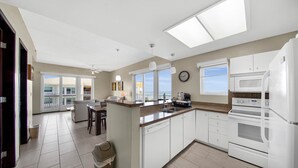 A modern kitchen with white appliances, a central island, and large windows.