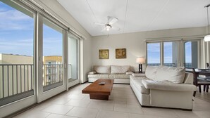 A spacious living room with a large sliding glass door, a ceiling fan, a wooden coffee table, and a beige sofa.