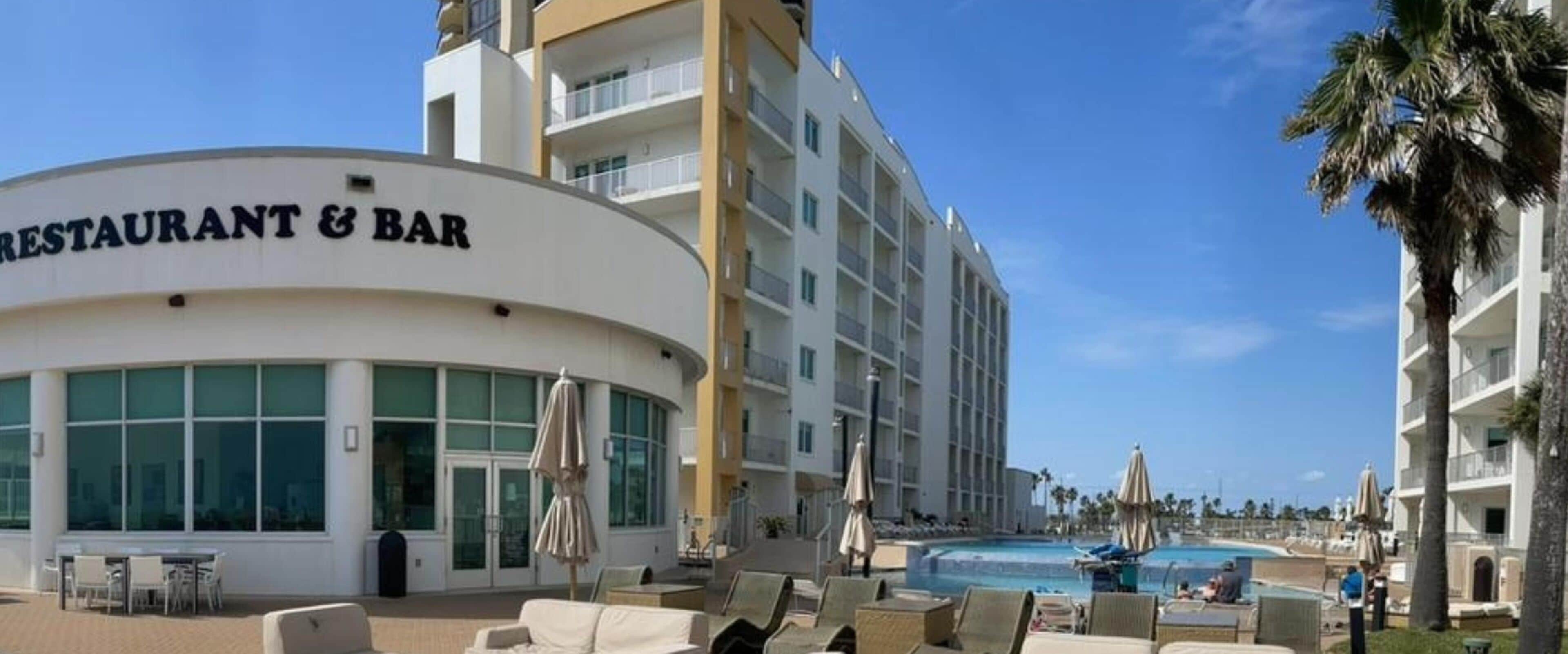 Un hotel con restaurante y bar, zona de piscina con sillones de descanso y una vista despejada del océano.