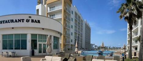 Un hotel con restaurante y bar, zona de piscina con sillones de descanso y una vista despejada del océano.