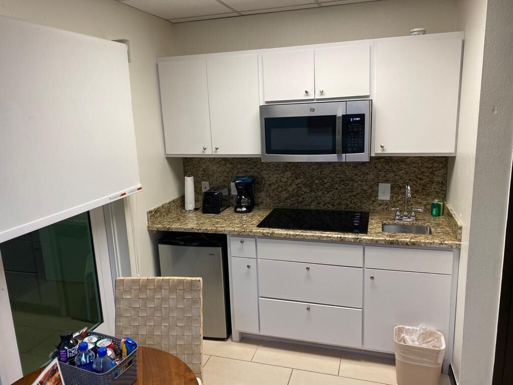 A compact kitchen with white cabinets, a built-in microwave, a coffee maker, and a trash bin.