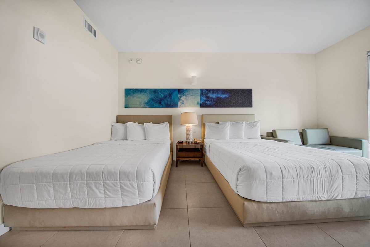 Une chambre d’hôtel avec deux lits, une table de chevet avec une lampe et des œuvres d’art abstraites accrochées au mur.