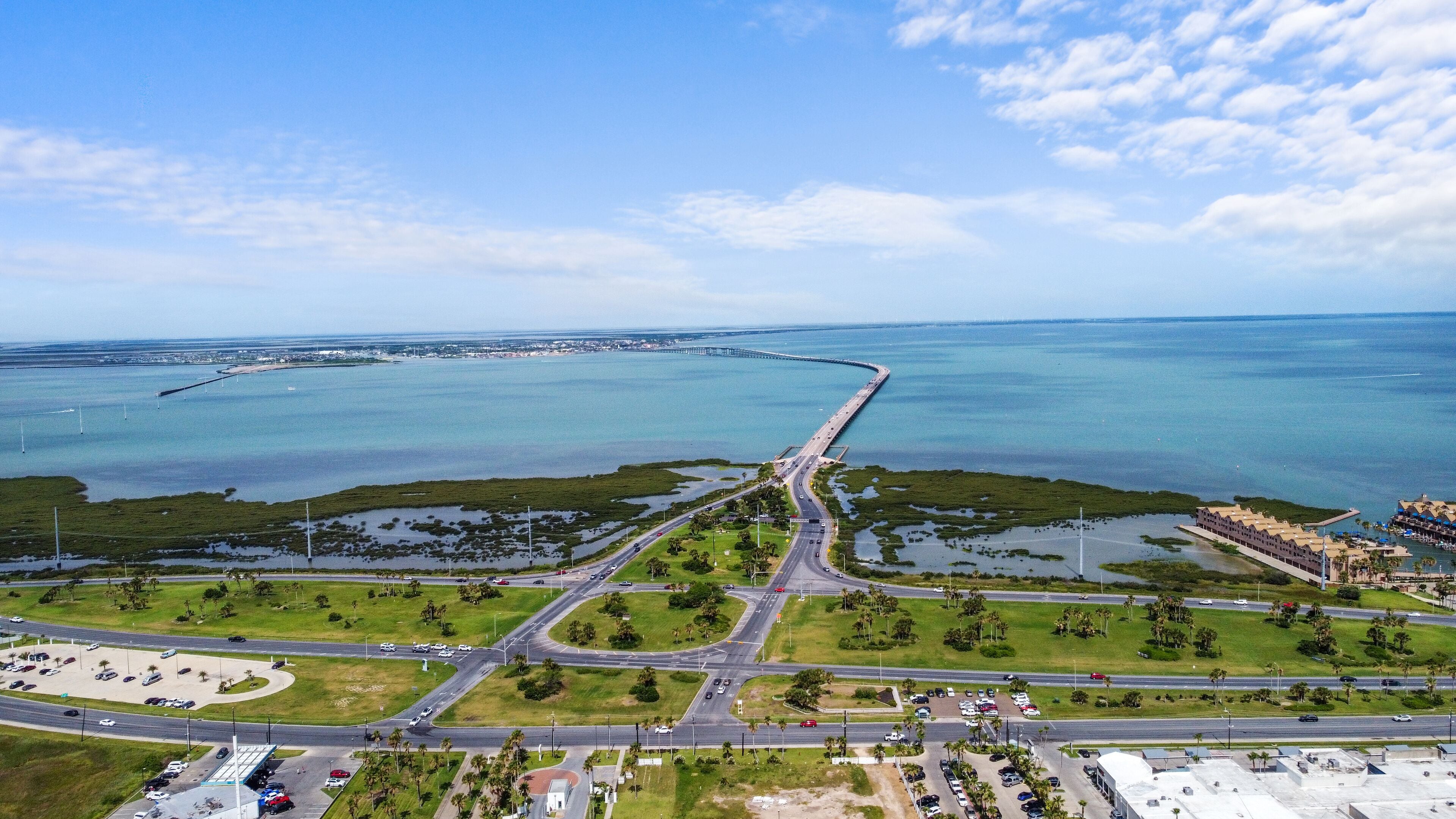 An aerial view of a coastal area with a bridge, roads, and a marina.