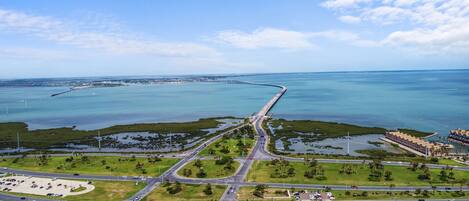 An aerial view of a coastal area with a bridge, roads, and a marina.