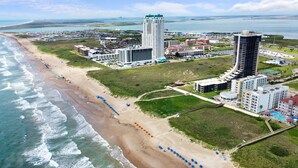 An aerial view of a coastal resort with beachfront properties, a high-rise hotel, and a marina.
