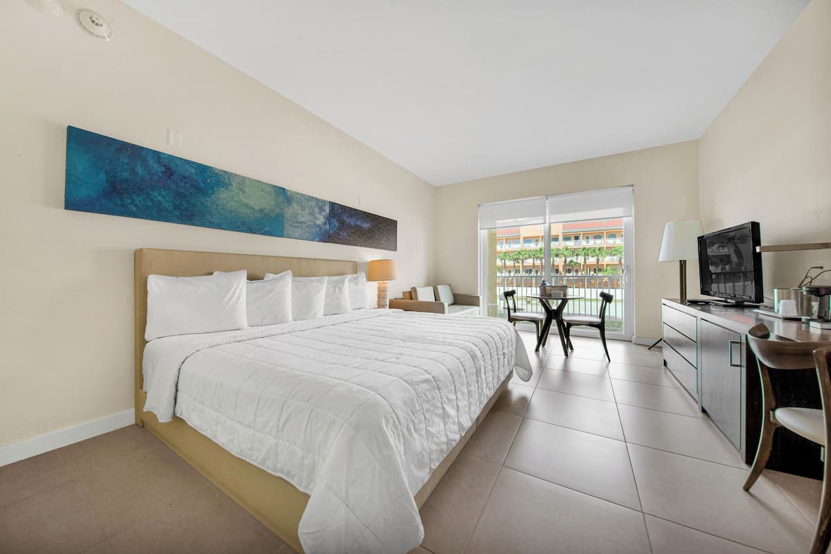 Une chambre d’hôtel avec un grand lit, un bureau avec une télévision et un balcon offrant une vue sur les palmiers.