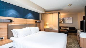 Une chambre d’hôtel dotée d’un grand lit, d’un bureau avec un ordinateur, d’une télévision et d’un coin salon comprenant un canapé et un fauteuil.