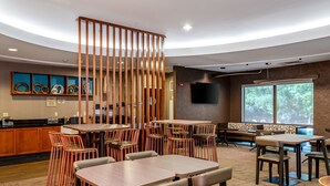 Un restaurante moderno con varias zonas de estar, un separador de madera y un amplio ventanal con vistas al exterior.