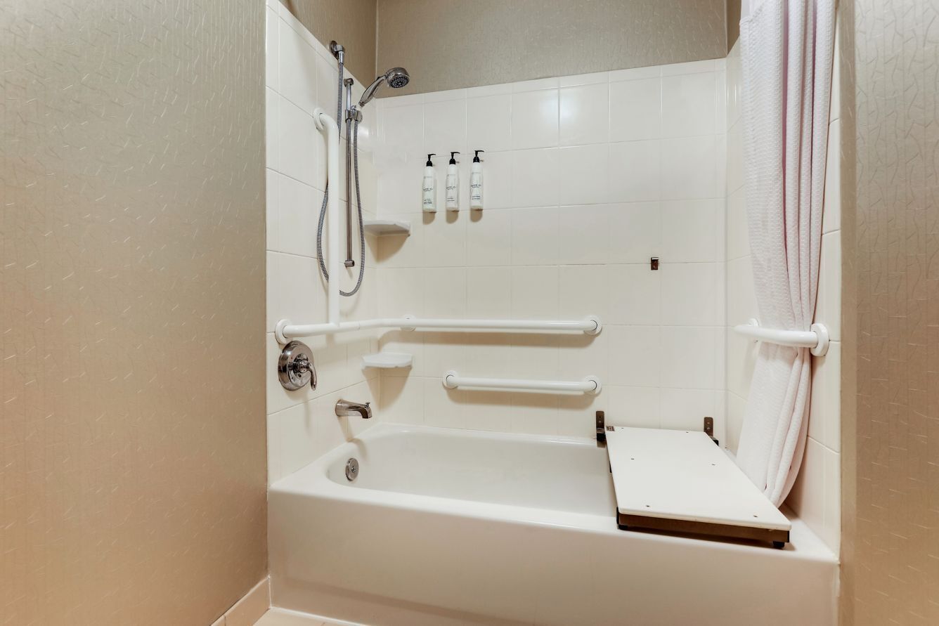 Une baignoire blanche équipée d’un pommeau de douche, de barres d’appui et d’un porte-serviettes.