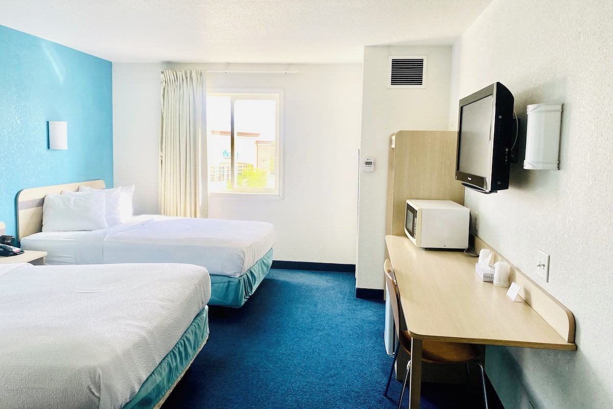 A hotel room with two beds, a desk with a television, and a window with curtains.