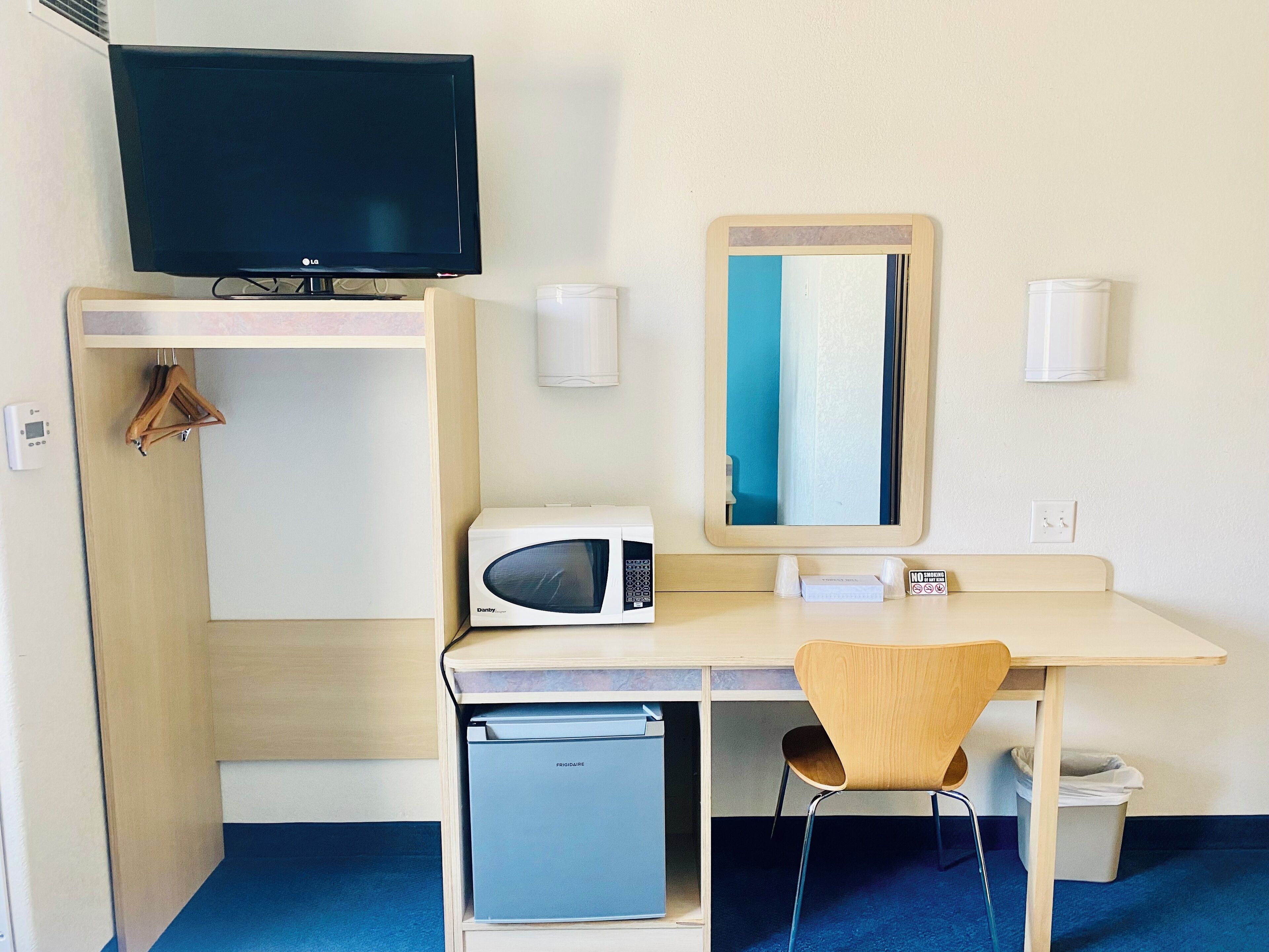 A hotel room with a television, microwave, mini-fridge, chair, and a mirror.