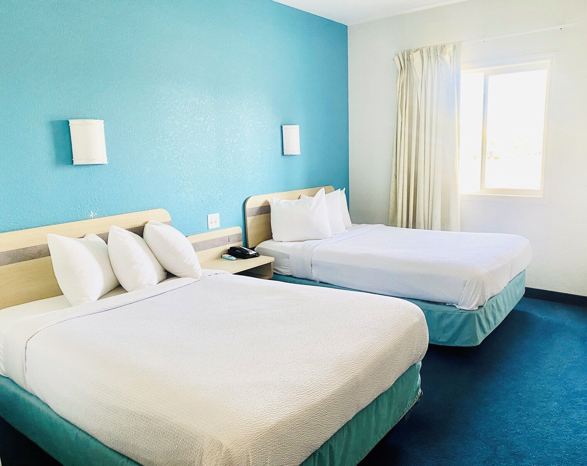 A hotel room with two beds, a nightstand, a telephone, and a window with curtains.
