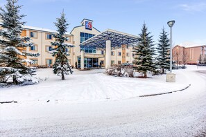 Un hotel con entrada cubierta de nieve, un espacio al aire libre techado y árboles cargados de nieve.