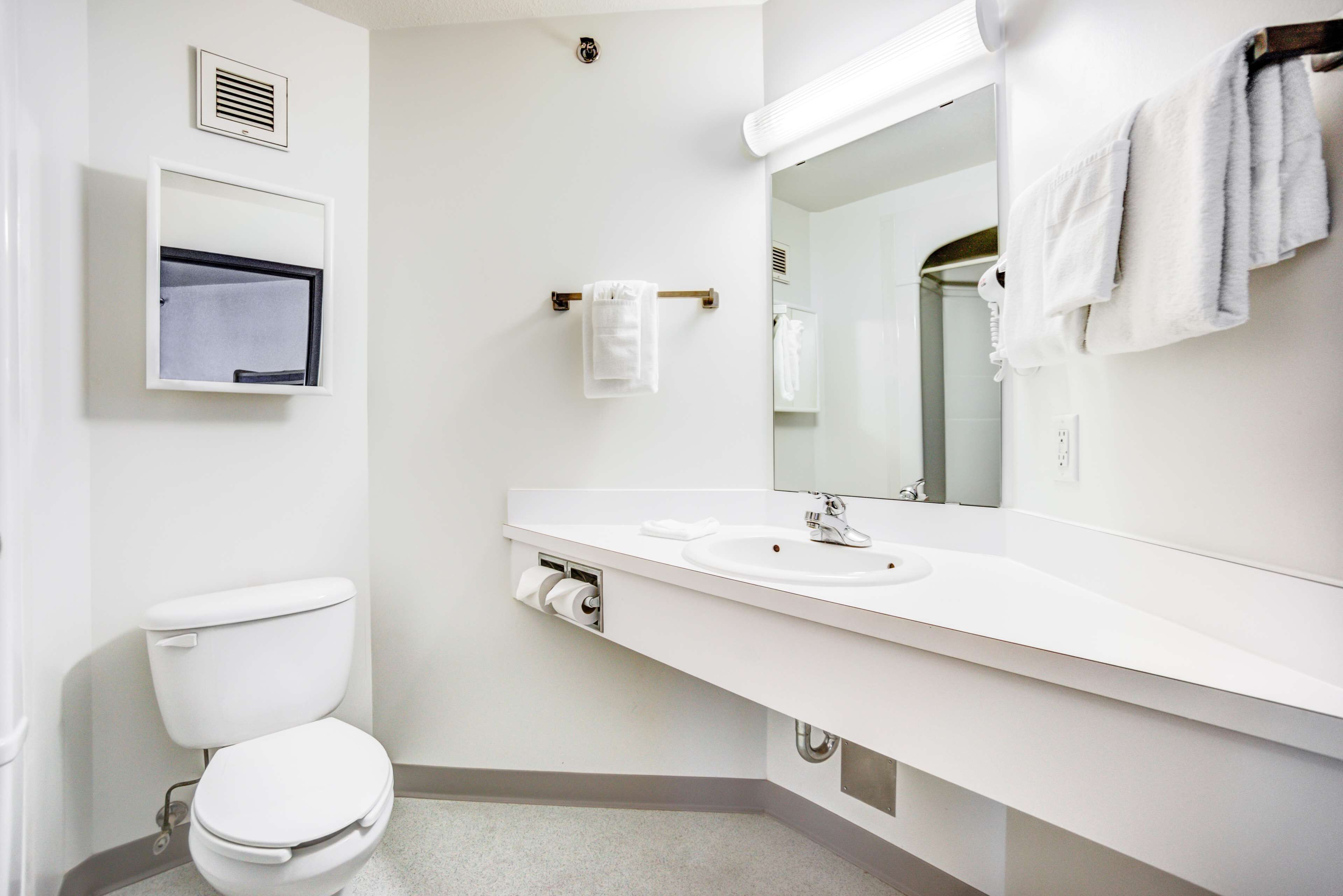 A modern bathroom with a toilet, sink, mirror, towel rack, and ventilation.