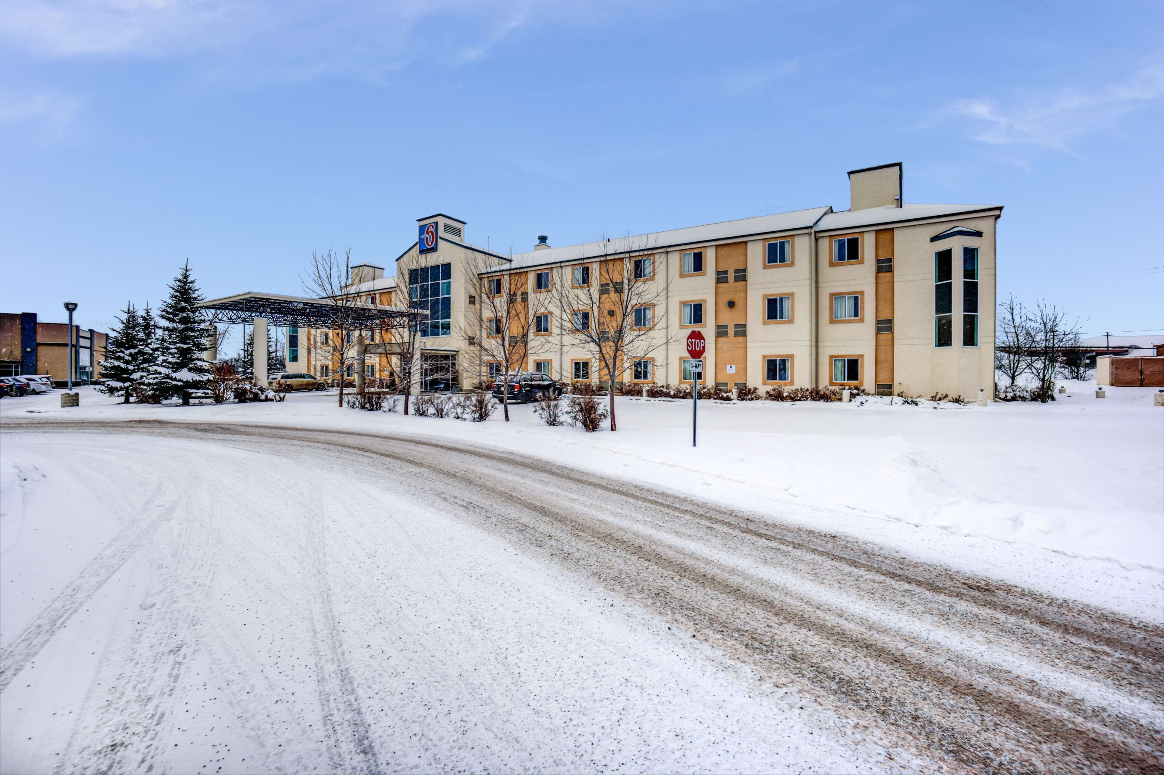 En byggnad med flera våningar, med ett stoppskylt framför, omgiven av snötäckt mark och träd.