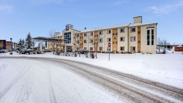 En byggnad med flera våningar, med ett stoppskylt framför, omgiven av snötäckt mark och träd.
