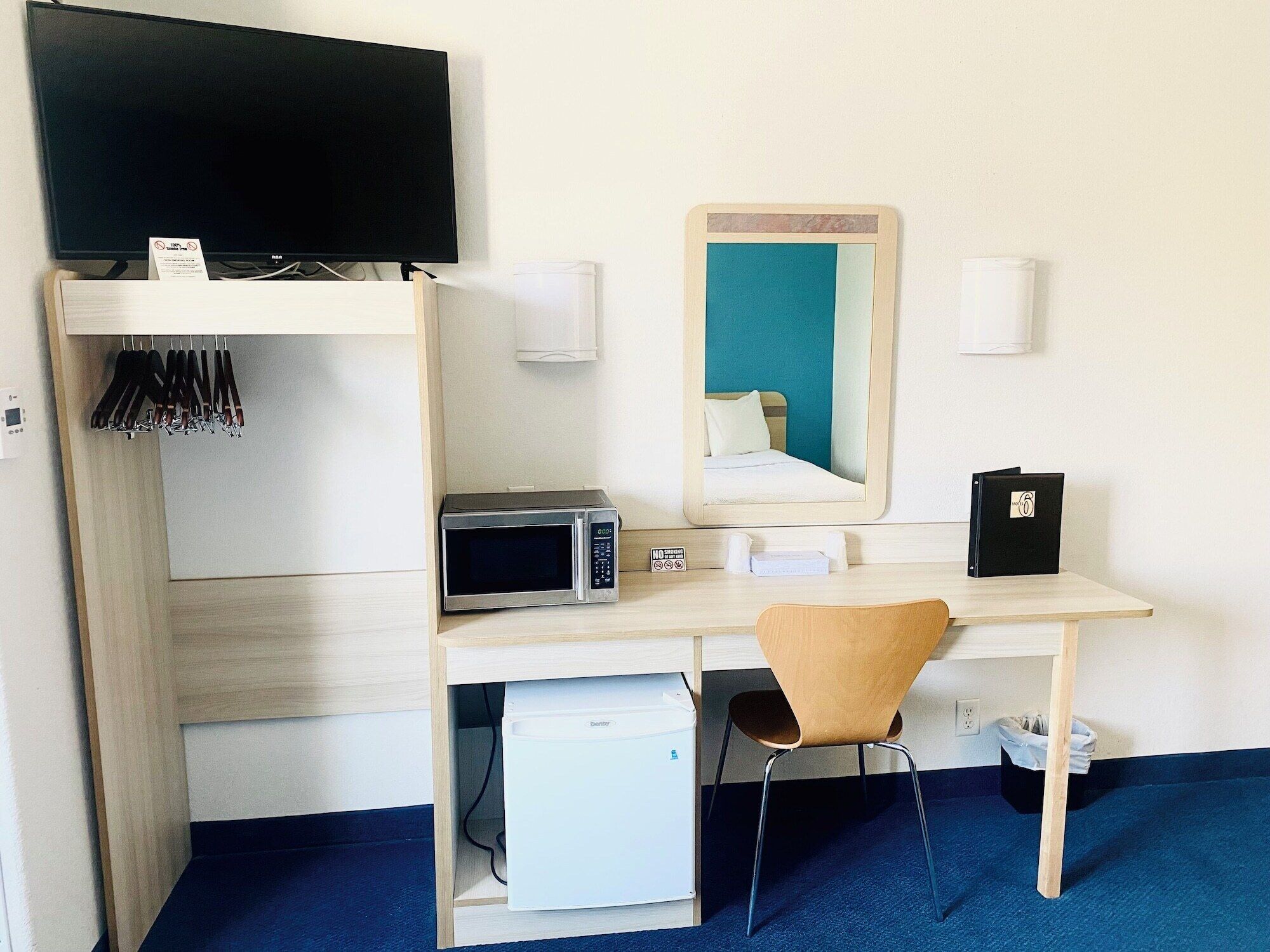 Camera d'albergo compatta con un letto, una scrivania con microonde, un piccolo frigorifero, una sedia, una TV e uno specchio.