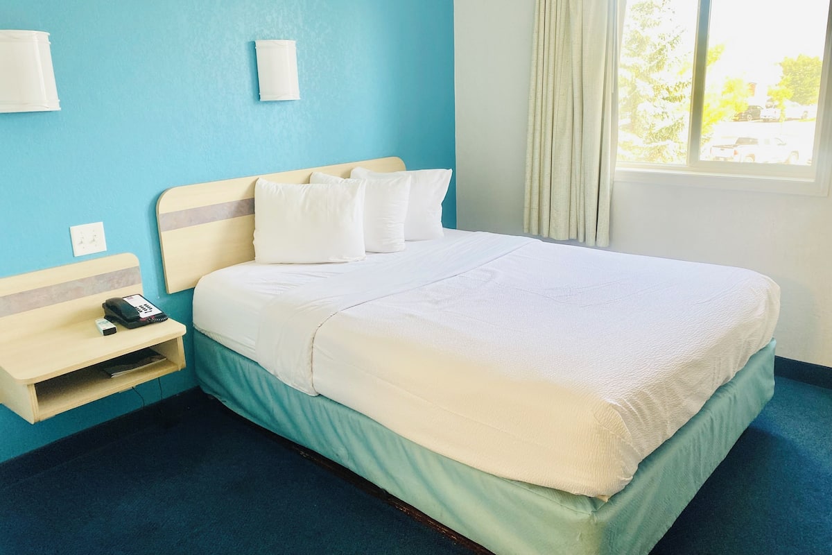 A hotel room with a bed, a bedside table with a phone, and a window with curtains.