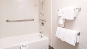 A bathroom with a bathtub, grab bars, a showerhead, and multiple white towels on a rack.