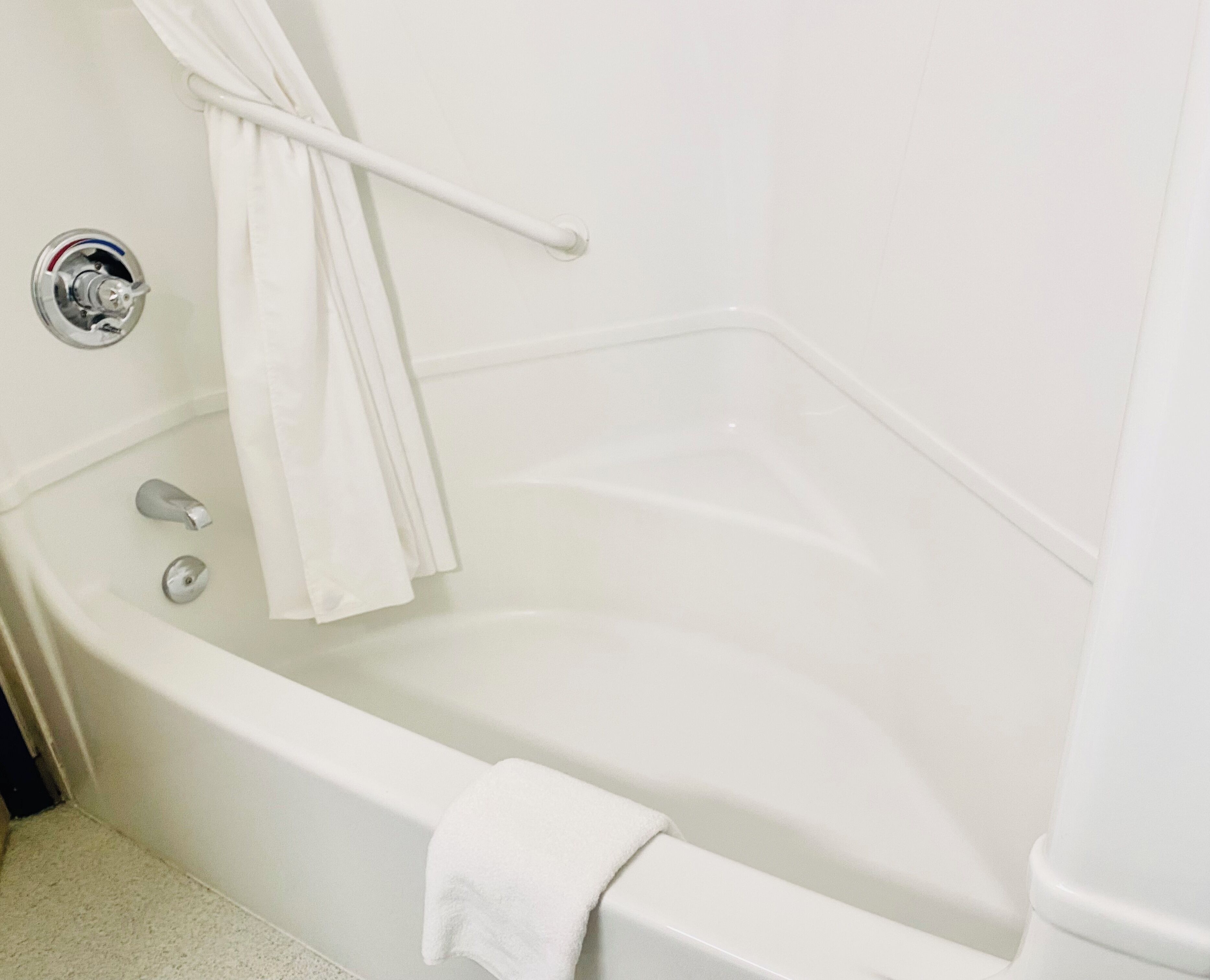 A white bathtub with a showerhead, a towel rack, and a towel hanging on the side.