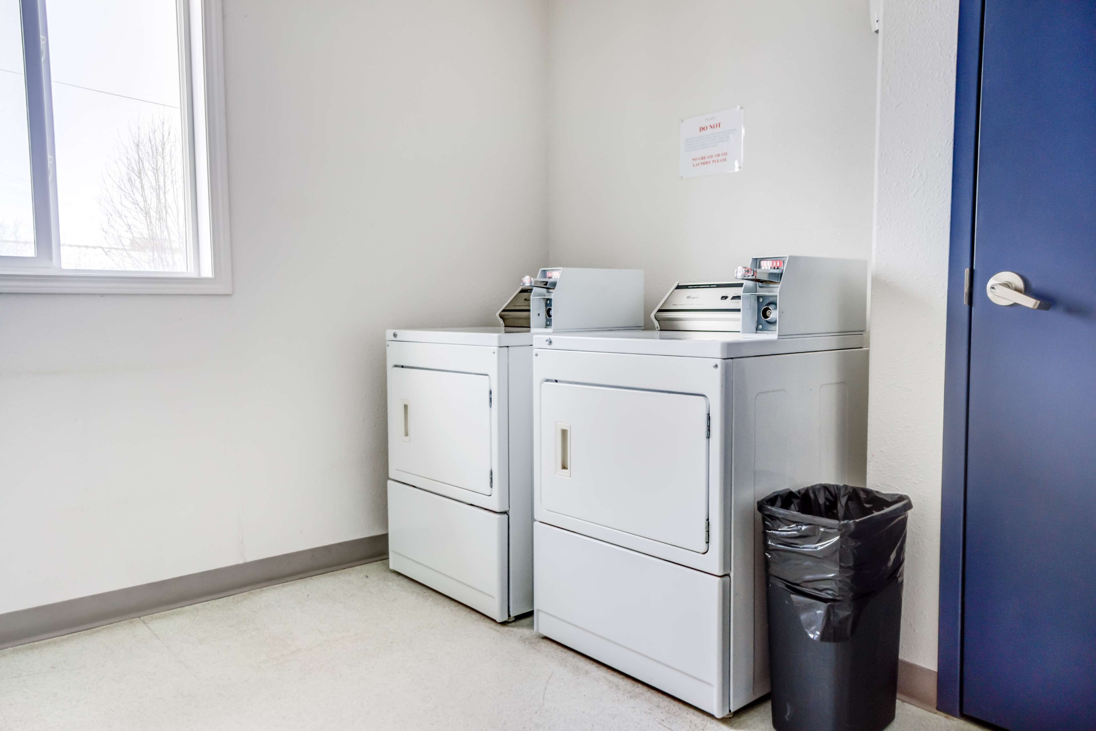 A laundry room with two stacked washers and dryers, a trash can, and a blue door.