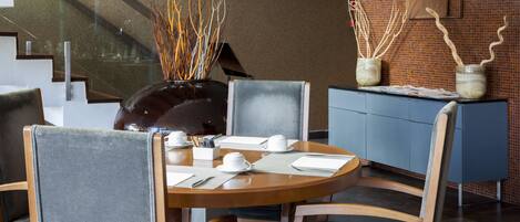 Un comedor con una mesa redonda, sillas y un florero con ramas decorativas.