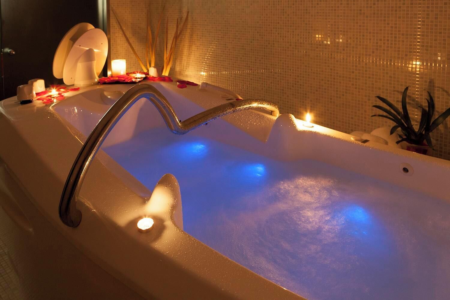 A bathtub with a built-in showerhead, surrounded by candles and decorative items.