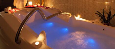 A bathtub with a built-in showerhead, surrounded by candles and decorative items.
