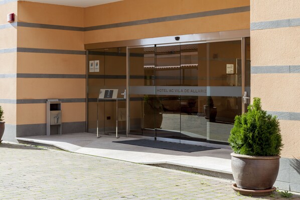A hotel entrance with a glass door, a potted plant, and a sign indicating the hotel name.