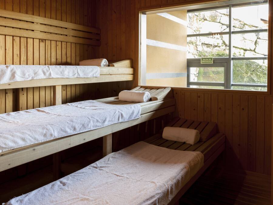 Uma cabana com paredes de madeira e uma janela. Há beliches com roupa de cama branca.
