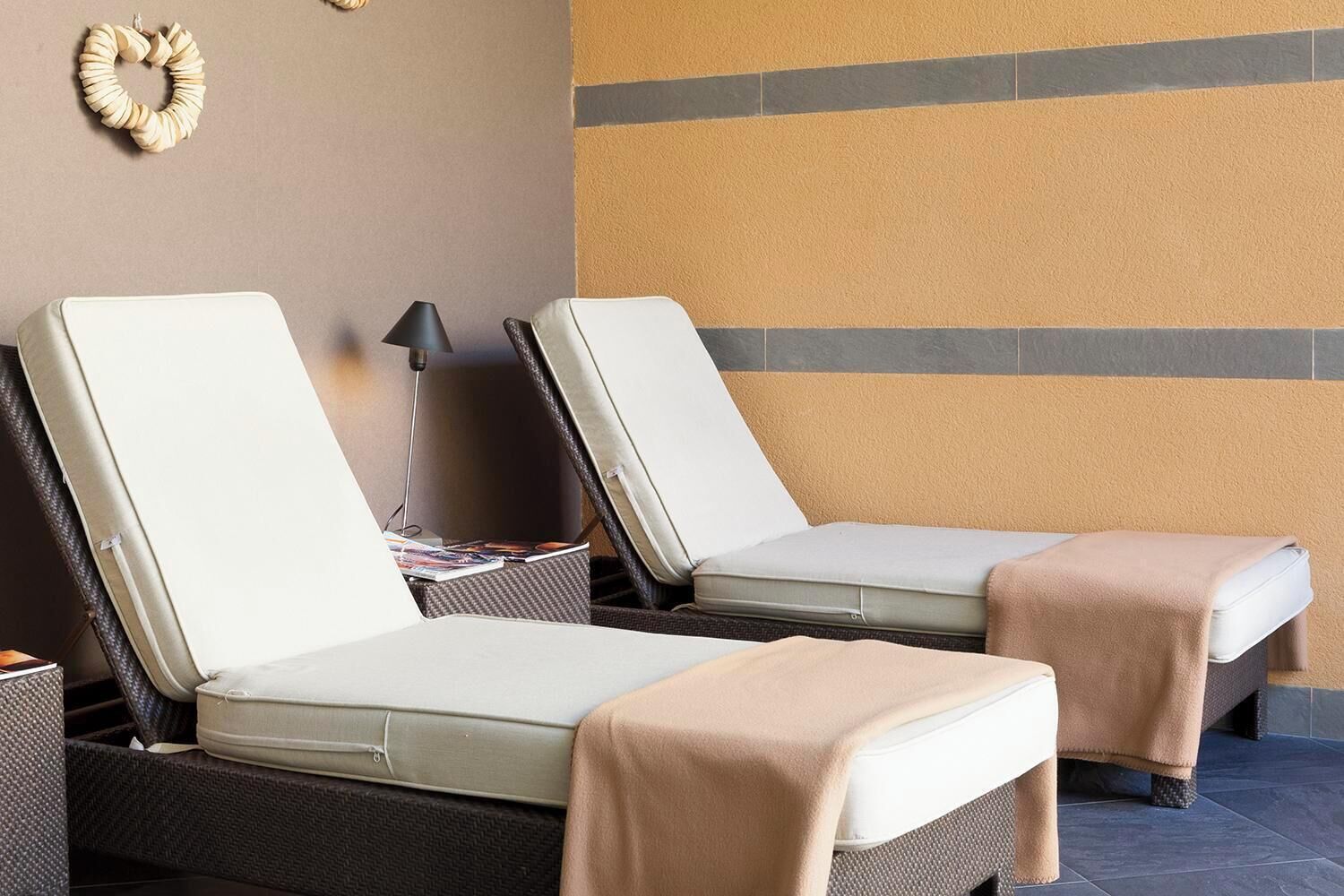 Two lounge chairs with cushions, a lamp, and a wall with a geometric pattern.