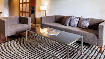 A modern hotel room with a sofa, armchair, and a glass coffee table.