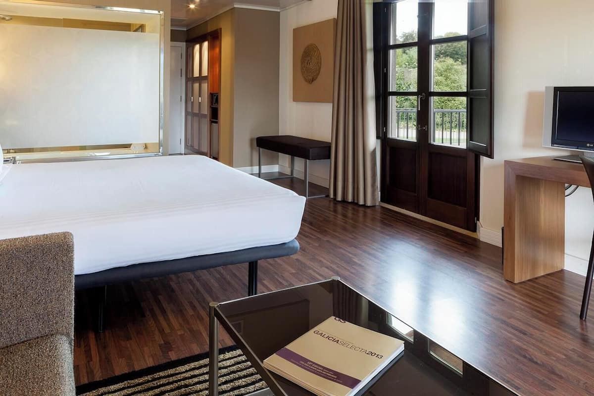 Une chambre d’hôtel avec un grand lit, un bureau, une chaise, une télévision et une fenêtre avec des rideaux.