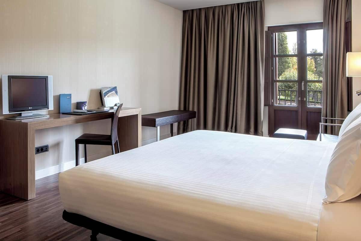 Une chambre d’hôtel avec un lit, un bureau, une chaise, une télévision et une fenêtre avec des rideaux.