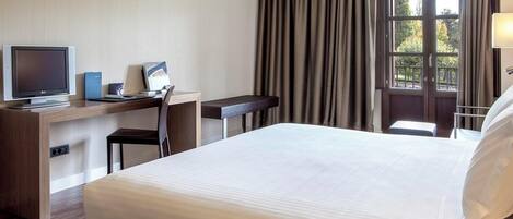 A hotel room with a bed, desk, chair, TV, and a window with curtains.