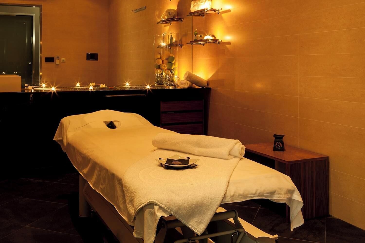 A massage table with a towel, a small table with a bottle, and a mirror.
