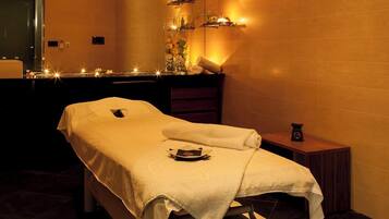 A massage table with a towel, a small table with a bottle, and a mirror.