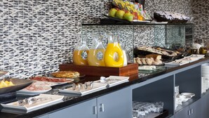 A buffet with various food items, including fruits, pastries, and beverages.