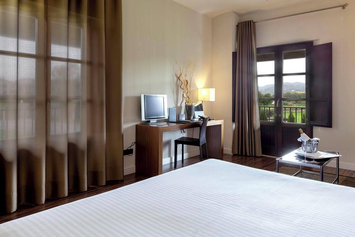 Une chambre d’hôtel équipée d’un lit, d’un bureau, d’un ordinateur, d’une lampe et offrant une vue sur l’extérieur.