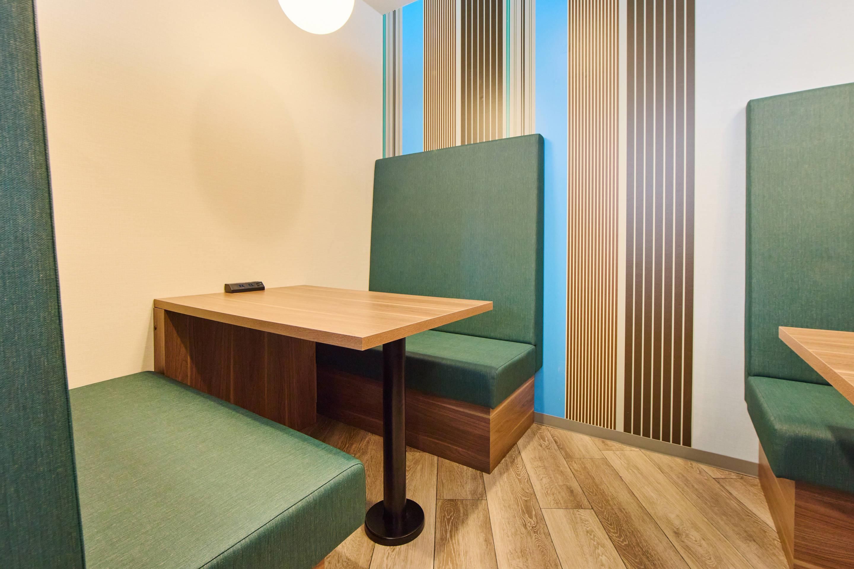 A corner seating area with a wooden table and green cushioned benches.