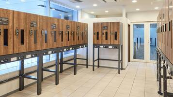 A row of wooden lockers with electronic keypads, a tiled floor, and a glass wall with natural light.
