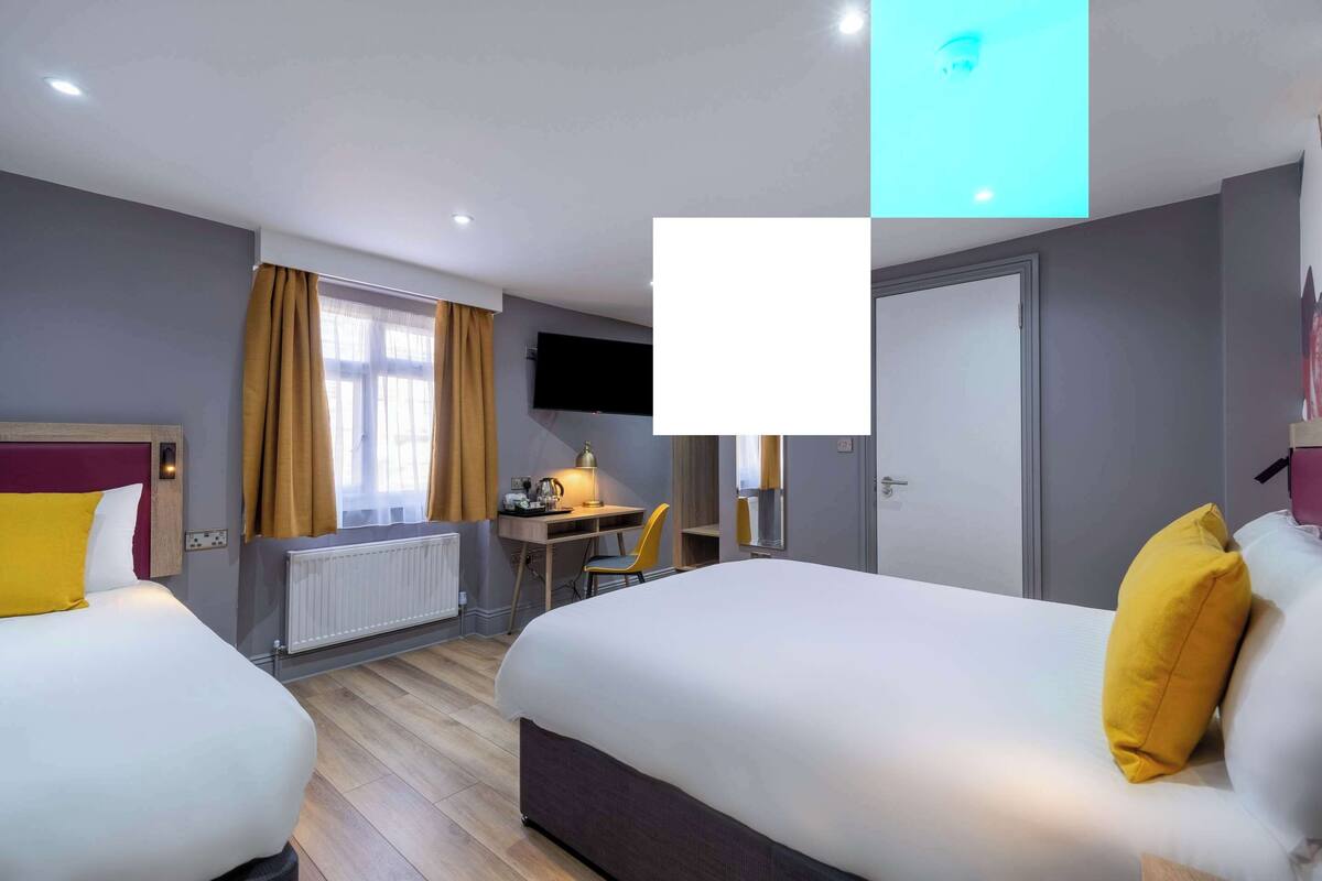A hotel room with two beds, a desk, a chair, a TV, and a radiator.