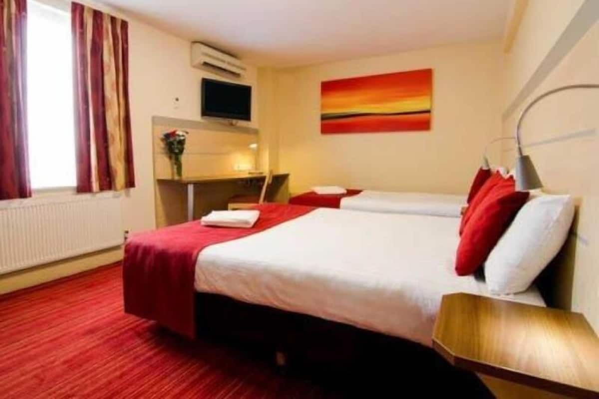 A hotel room with two beds, a desk, a TV, and a painting on the wall.