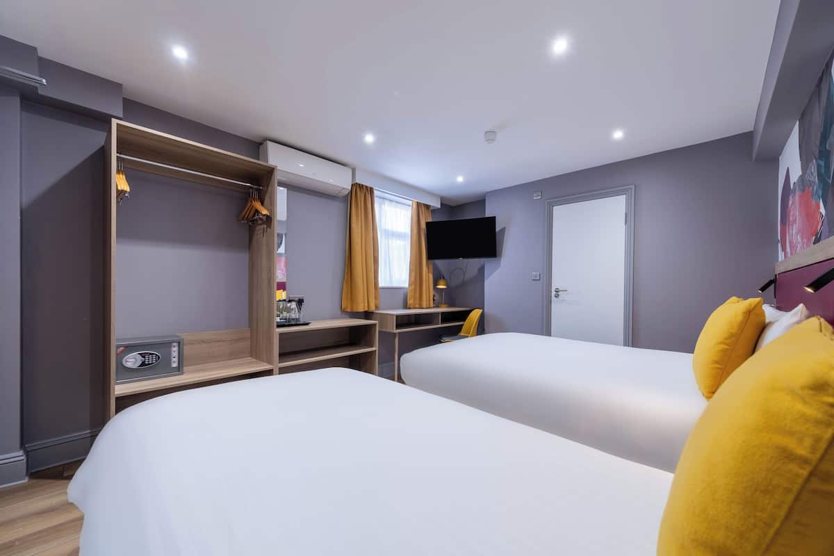 A hotel room with two beds, a desk, a TV, and a wardrobe.