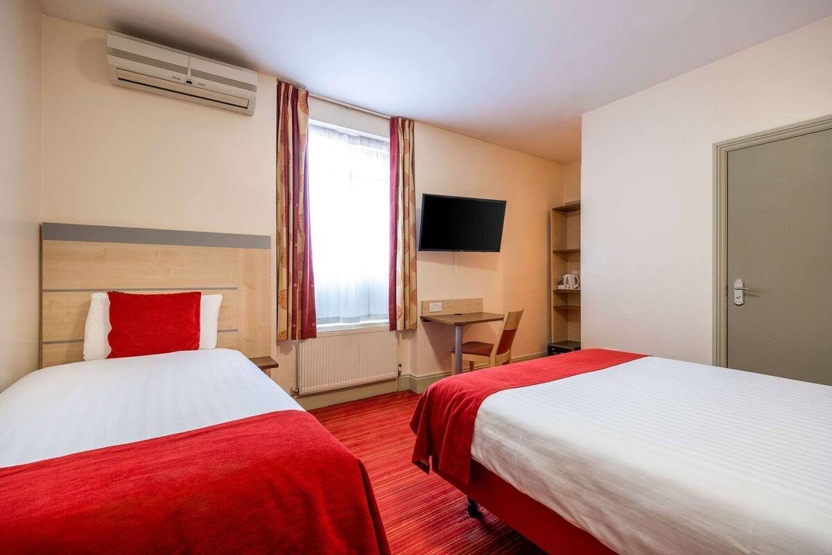 Ein Hotelzimmer mit zwei Betten, einem Fernseher, einem kleinen Tisch und einem Sessel.